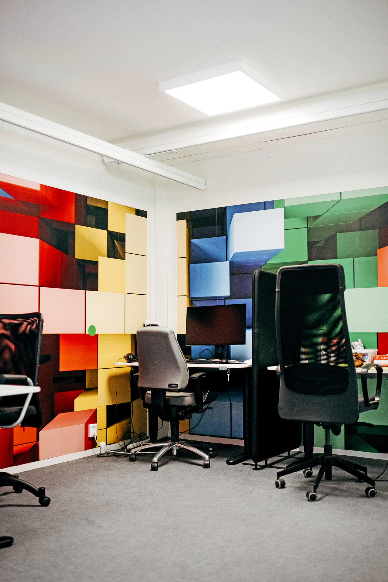 Arbetsrum med skrivbord, kontorsstolar och datorer. Väggarna är täckta av färgglada, geometriska mönster som skapar en kreativ och lekfull miljö.