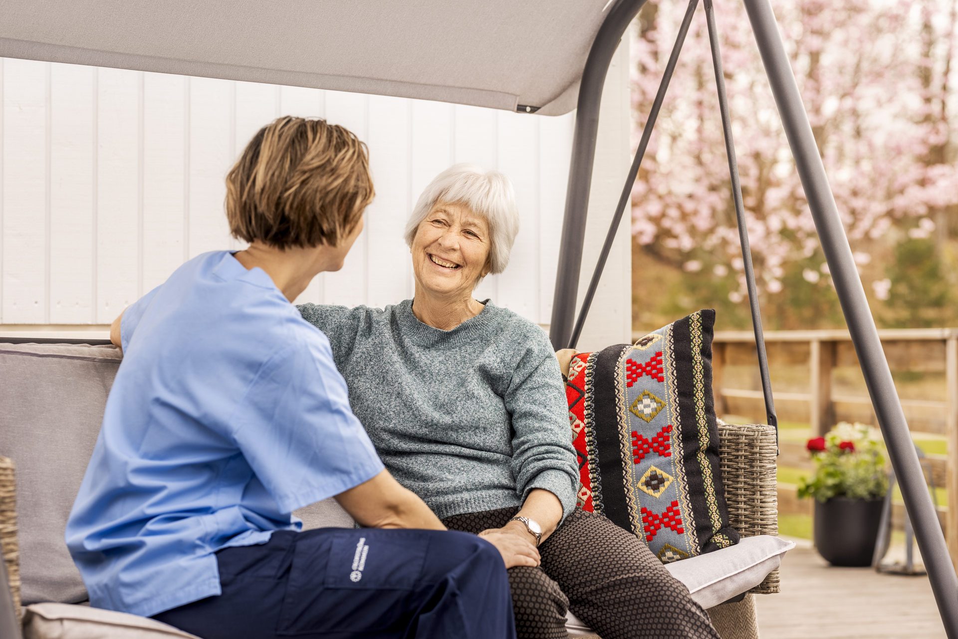 En boende och omsorgspersonal sitter tillsammans utomhus vid Borggården demensvård i Olofström. De samtalar på en uteplats som ingår i en modullösning från Expandia.