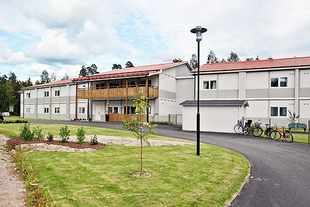 Boendemoduler från Expandia för Vidingehem Bo med rött sadeltak, placerade i grön utemiljö med gångvägar, cyklar och planteringar.