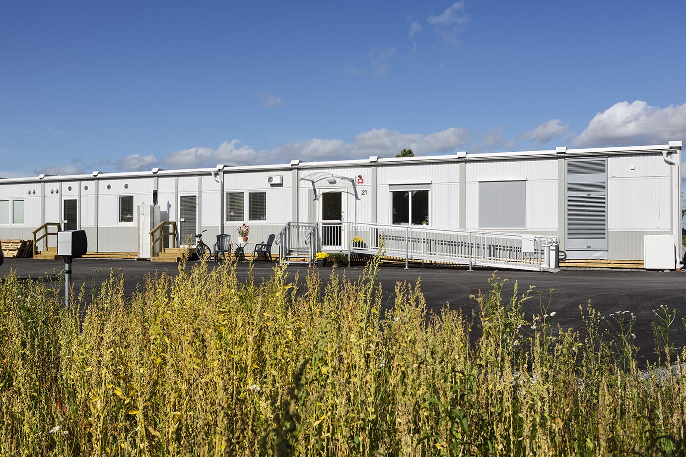 Nordrona LSS-boende i Norrtälje med vita boendemoduler från Expandia placerade i grön naturmiljö med ängsmark och blå himmel.